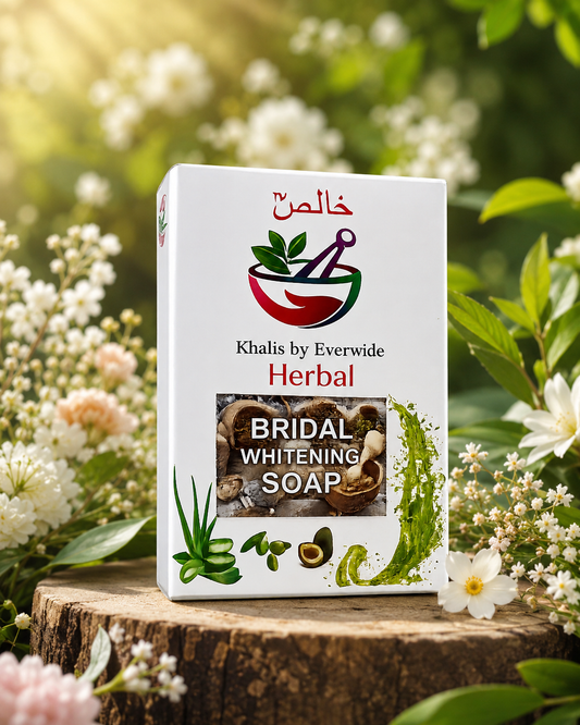 A boxed herbal soap product standing on a tree stump outdoors, surrounded by white flowers and green foliage. The front of the box reads 'Khalis by Everwide Herbal Bridal Whitening Soap' with a red and green mortar-and-pestle logo and botanical illustrations.